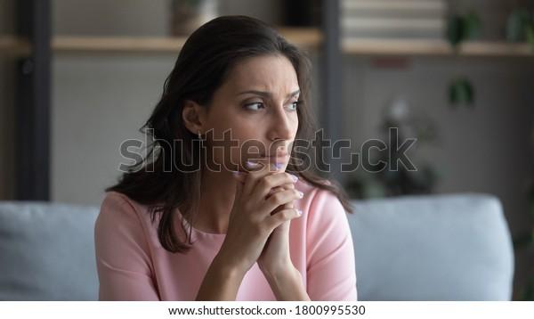 擔心年輕的印度阿拉伯婦女坐在家裡的沙發上看遠處思考，焦慮、不開心、不開心、阿拉伯混血兒、女性患有精神心理、個人問題、哀悼或嚮往